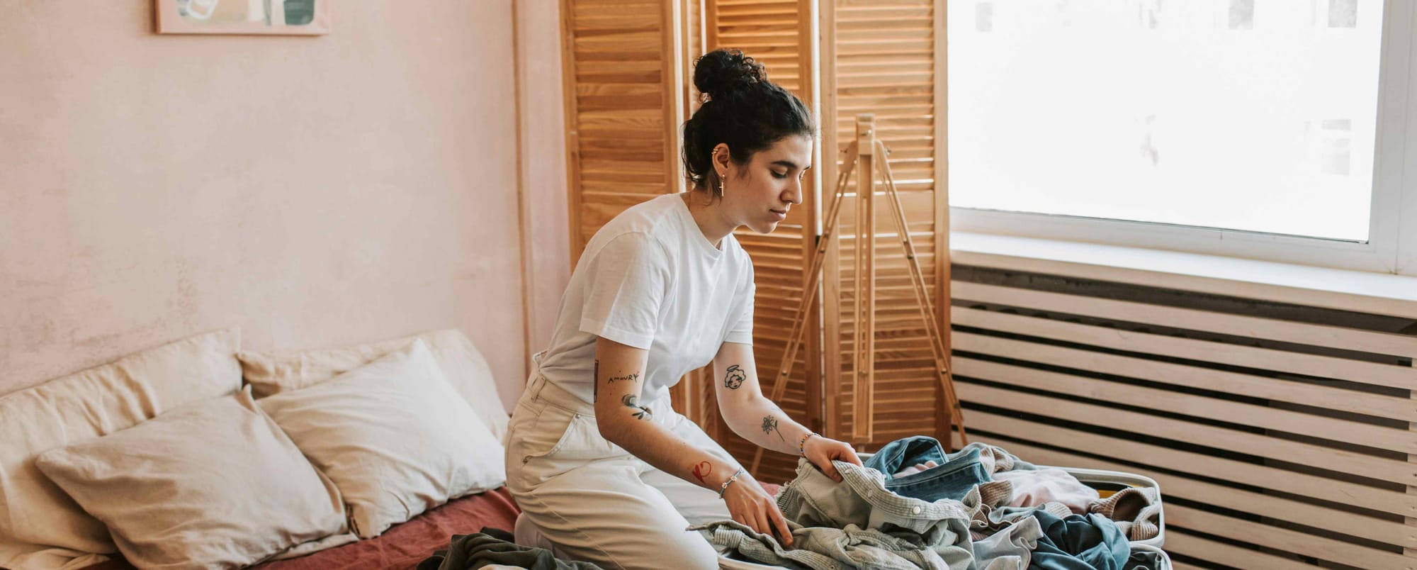 Seorang wanita sedang menyusun pakaian di kopernya.