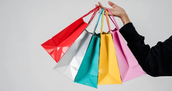 Gambar tangan kanan memegang 5 paper bag berwarna merah, perak, tosca, kuning, dan pink